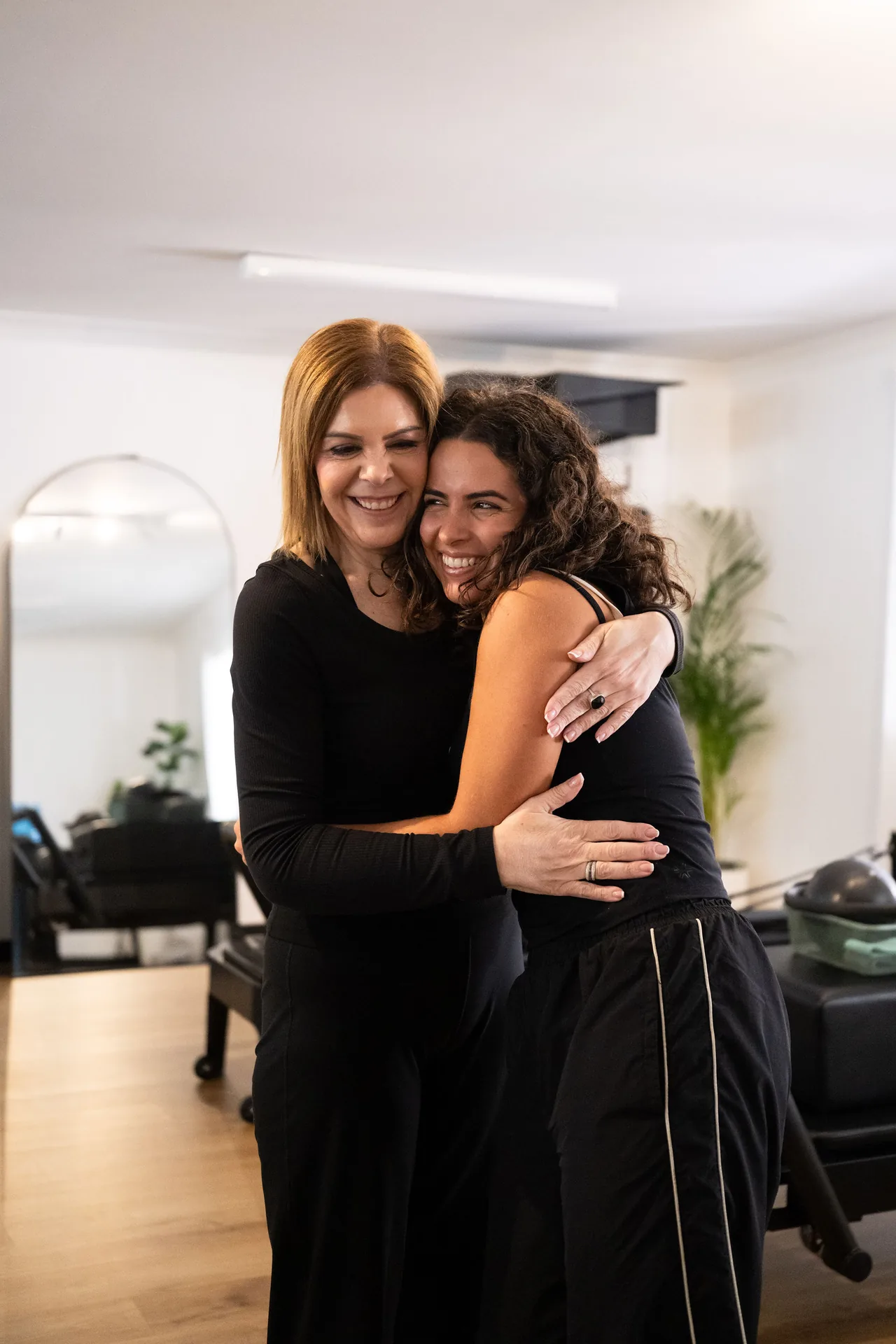 Two women sharing a friendly embrace at BASE Pilates Collective