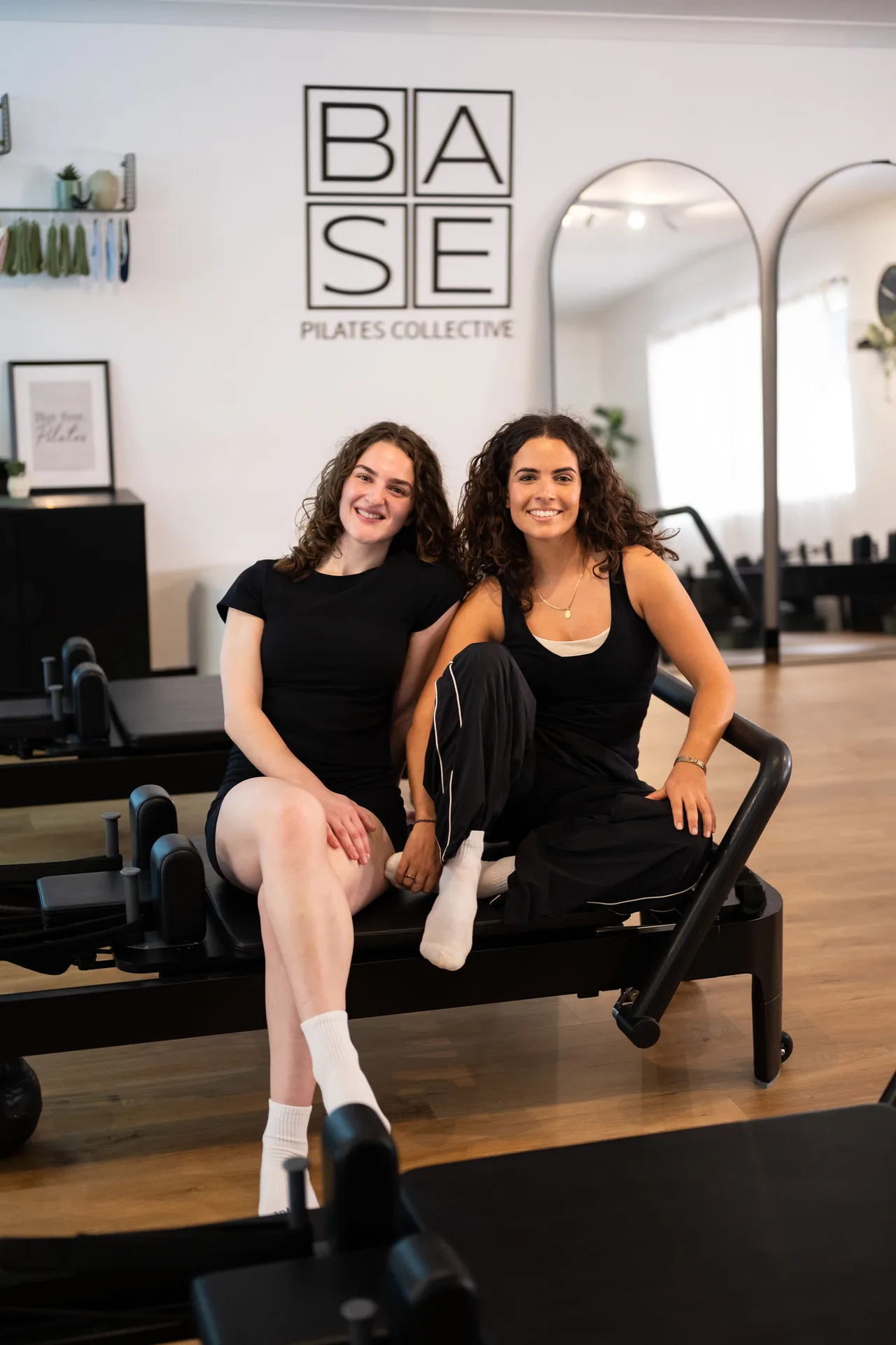Two women seated together on a reformer at BASE Pilates